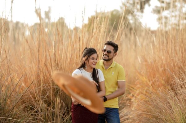 A couple enjoying a romantic pre-wedding shoot in Jaipur, surrounded by golden tall grass, with a warm sunset glow in the background.