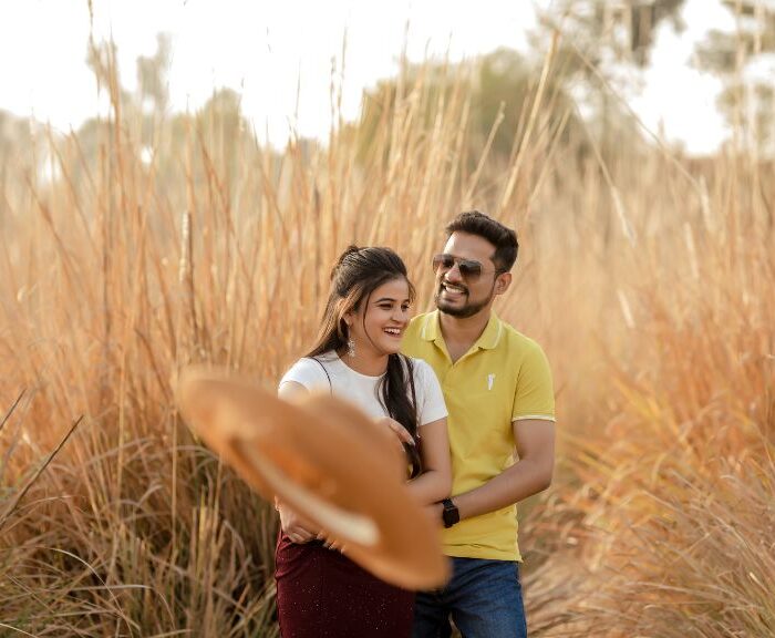 A couple enjoying a romantic pre-wedding shoot in Jaipur, surrounded by golden tall grass, with a warm sunset glow in the background.