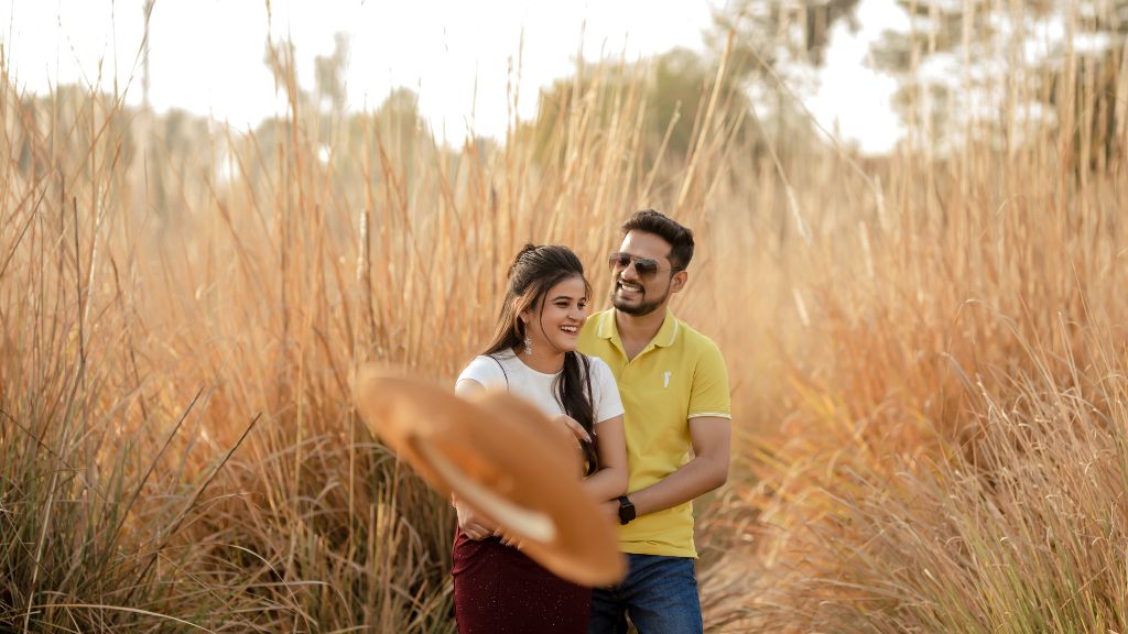 A couple enjoying a romantic pre-wedding shoot in Jaipur, surrounded by golden tall grass, with a warm sunset glow in the background.