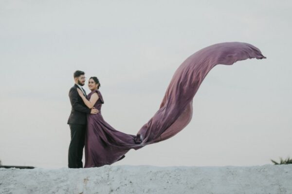 A couple embracing during a pre-wedding shoot in Jaipur, with the bride’s flowing gown creating a stunning visual against a dreamy sky backdrop.