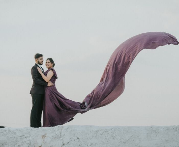 A couple embracing during a pre-wedding shoot in Jaipur, with the bride’s flowing gown creating a stunning visual against a dreamy sky backdrop.