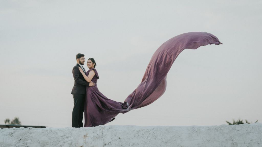 A couple embracing during a pre-wedding shoot in Jaipur, with the bride’s flowing gown creating a stunning visual against a dreamy sky backdrop.