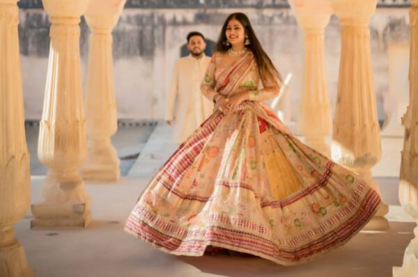 A couple during a pre-wedding shoot in Jaipur, with the bride twirling in a colorful lehenga, while the groom walks behind her in a cream-colored outfit.