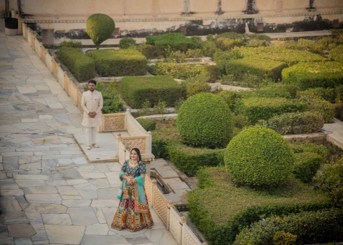 A pre-wedding couple photoshoot in a beautifully manicured garden, with the bride in a colorful lehenga and the groom in traditional attire standing in a serene and picturesque setting