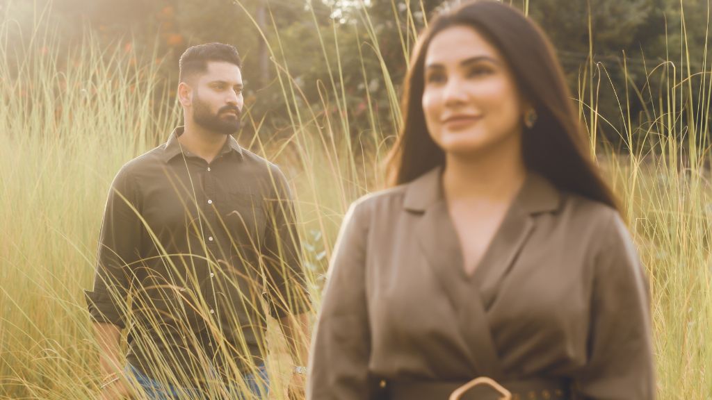 A couple poses for a pre-wedding shoot in Jaipur, with a serene natural backdrop featuring tall grass and soft lighting.