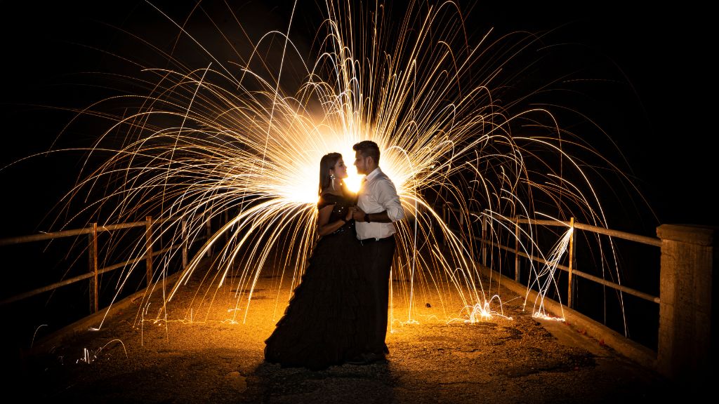 A couple embraces under a shower of sparks during their pre-wedding shoot in Jaipur at night.