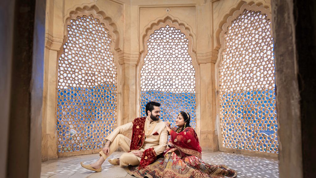 A couple poses in traditional attire during their pre-wedding shoot in Jaipur, sitting on the floor inside a beautiful architectural space.