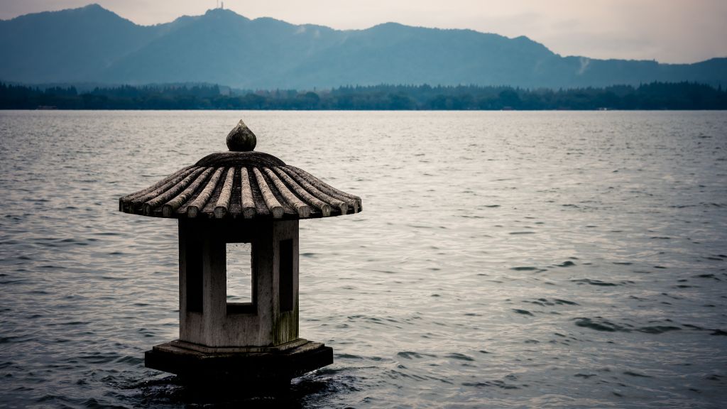 A peaceful scene of a small pagoda on the water, with mountains in the background, perfect for a pre-wedding shoot location.