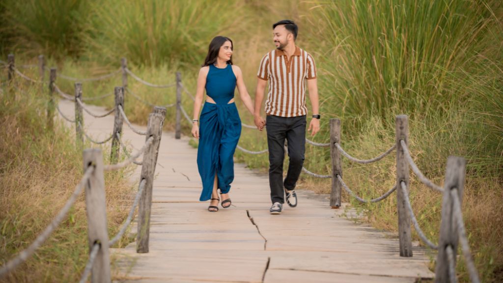  A couple holding hands, walking down a wooden pathway in a lush grassy area during a pre-wedding shoot in Jaipur.