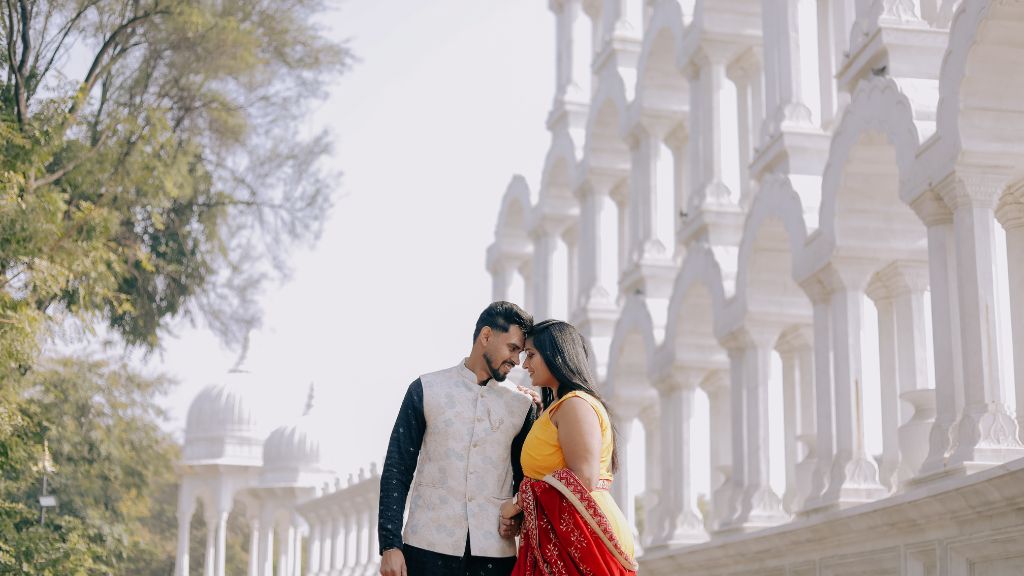 A couple gazing at each other near a white marble structure during a pre-wedding shoot in Jaipur, with beautiful arches in the background.