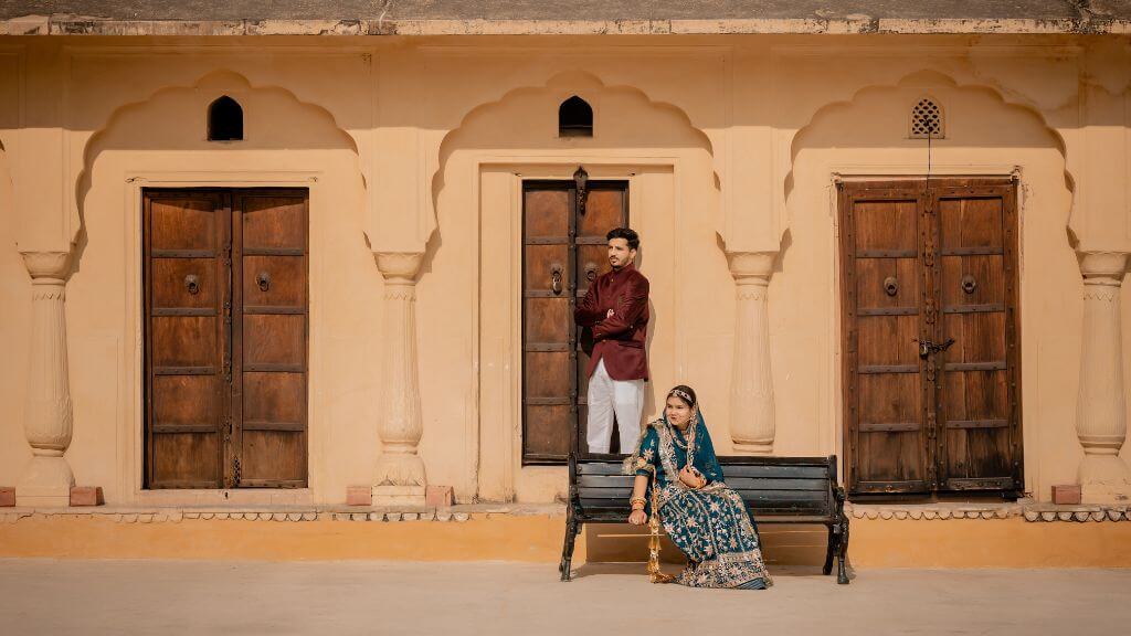 Couple posing during pre wedding shoot in Jaipur in front of a traditional Rajasthani haveli with wooden doors and sandstone walls.