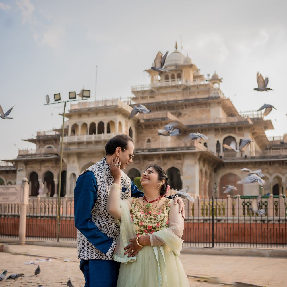 Couple embracing each other, laughing joyfully, with the Albert Hall Museum in the background and pigeons flying around them during a post-wedding photoshoot in Jaipur.