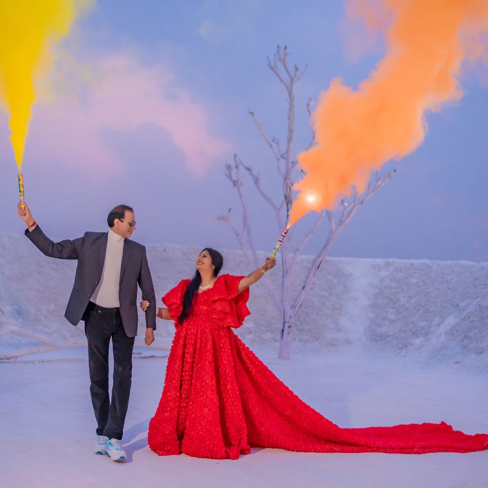 Couple holding colorful smoke flares, walking hand in hand, surrounded by a white landscape during a post-wedding photoshoot in Jaipur.