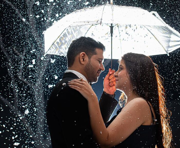 A couple embraces under an umbrella during a pre-wedding shoot in Jaipur, with snow-like sparkles falling around them, creating a romantic atmosphere.