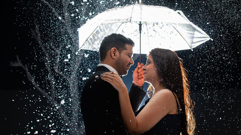 A couple embraces under an umbrella during a pre-wedding shoot in Jaipur, with snow-like sparkles falling around them, creating a romantic atmosphere.