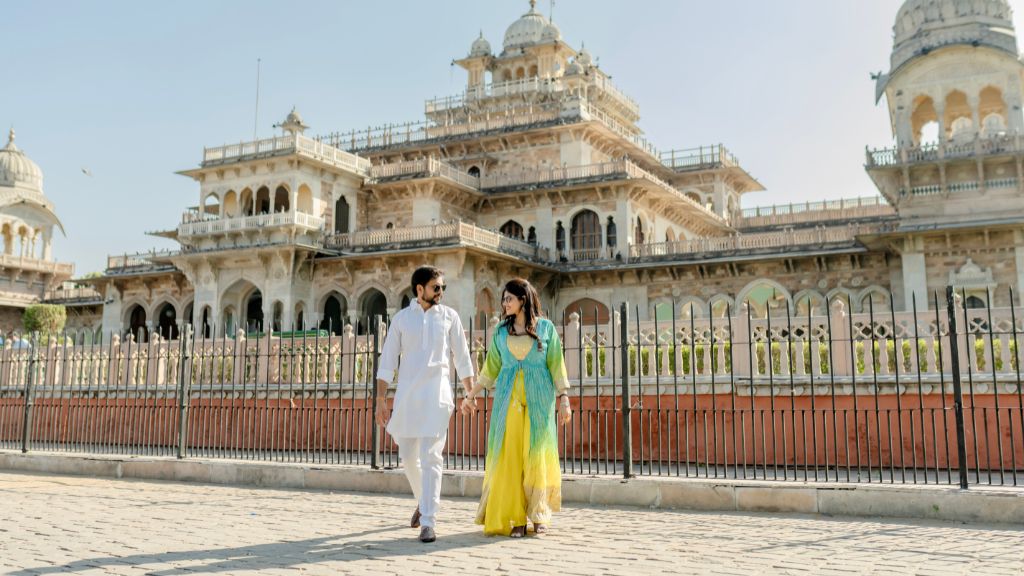 A couple holding hands during a pre-wedding shoot in Jaipur, with the magnificent architecture of the monument in the background.