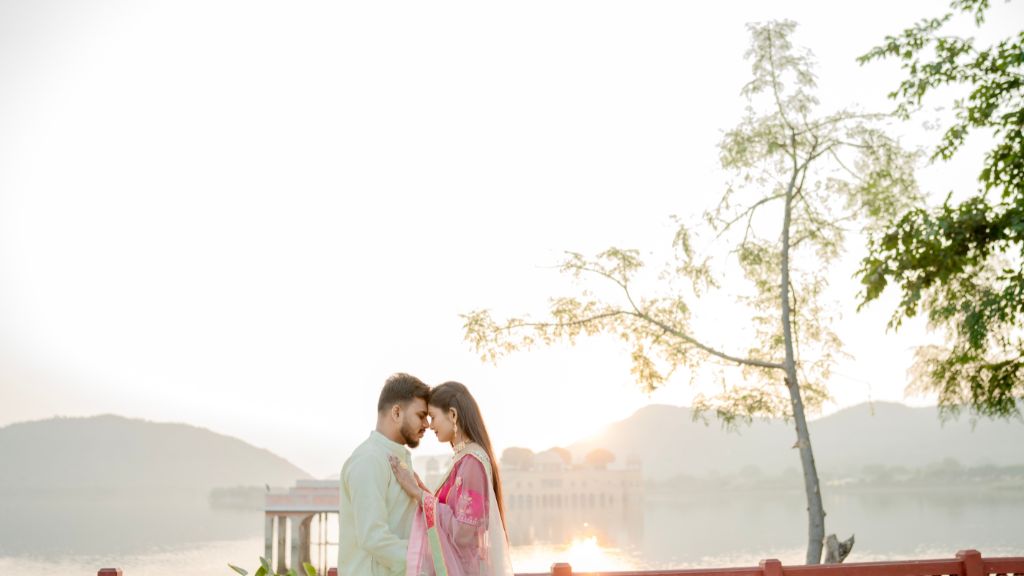 Couple embracing during a pre-wedding shoot in Jaipur with a serene backdrop of mountains and a water body.