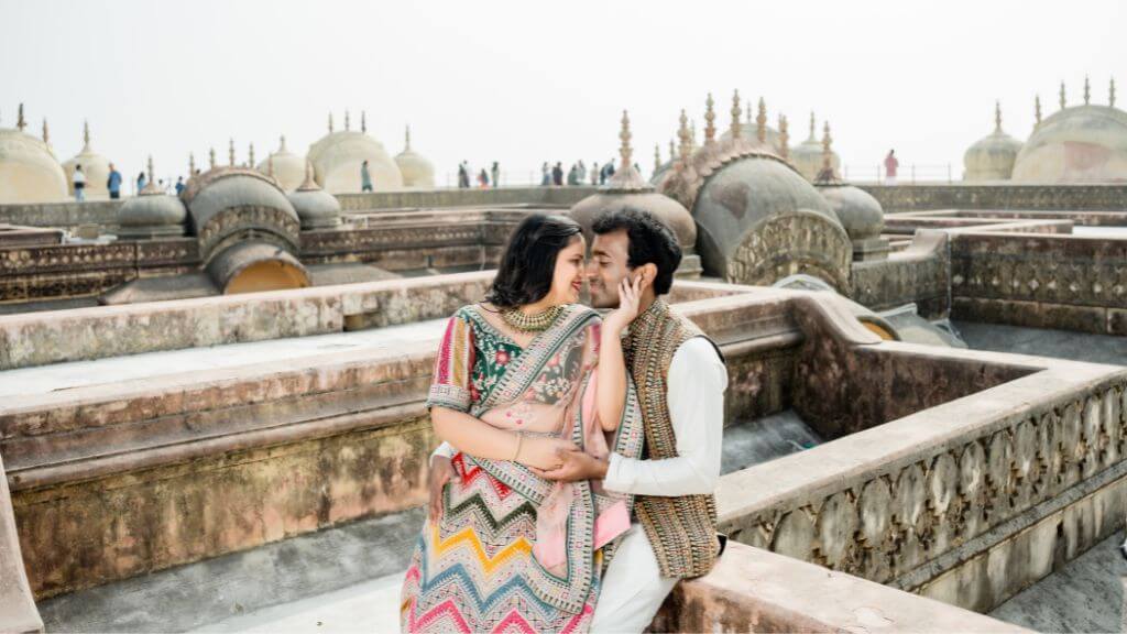 Couple in colorful ethnic outfits sharing a romantic moment on a historic rooftop, showcasing vibrant pre wedding shoot outfit ideas.