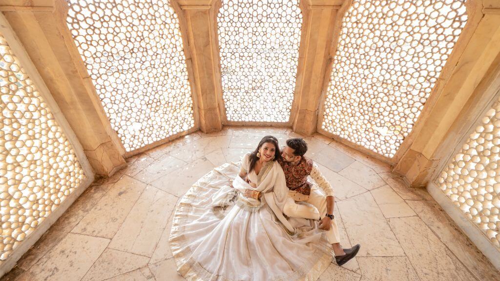 Couple in traditional outfits sitting under golden jharokha windows during a pre wedding photoshoot in Jaipur studio
