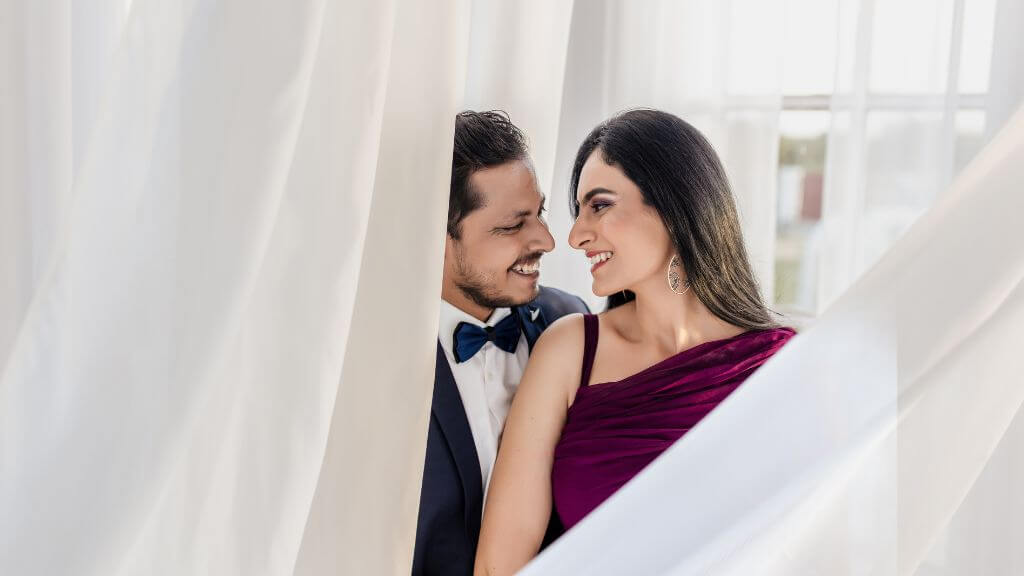 Couple posing romantically behind white curtains in natural soft light during ideal Pre Wedding Shoot Timing in Jaipur.