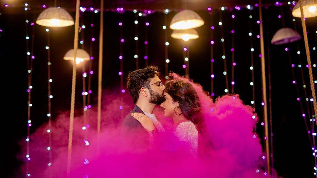 Couple posing under fairy lights with pink smoke at night during a creatively timed Pre Wedding Shoot in Jaipur.