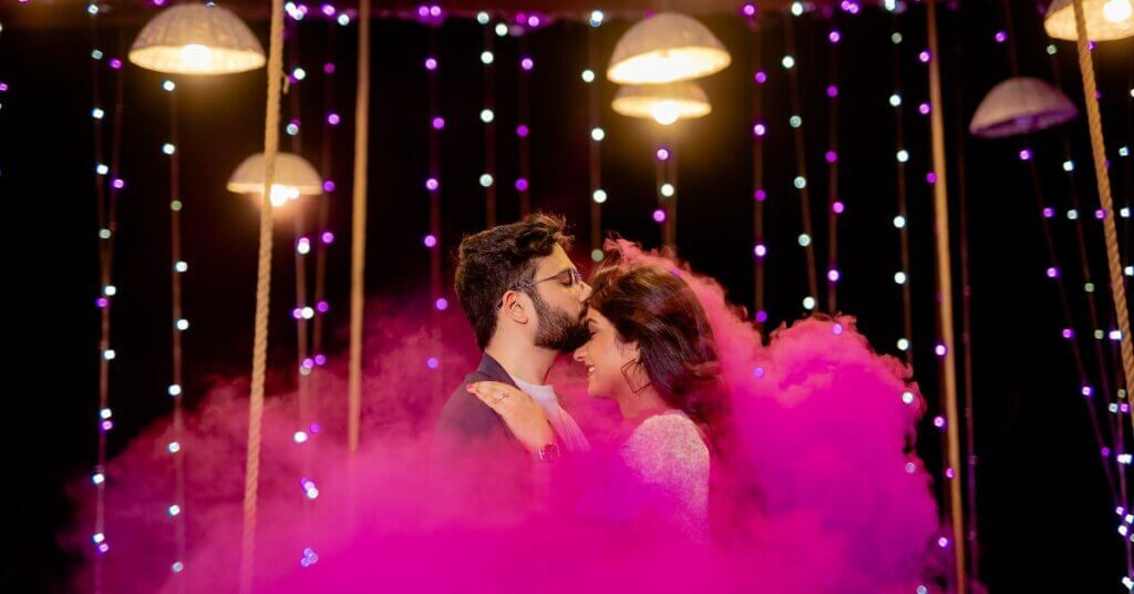 Couple sharing a romantic moment under fairy lights and colored smoke during a night Pre Wedding Shoot Timing in Jaipur.