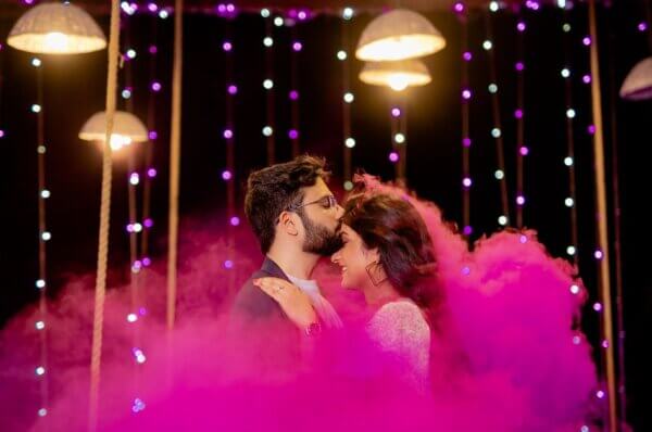 Couple sharing a romantic moment under fairy lights and colored smoke during a night Pre Wedding Shoot Timing in Jaipur.