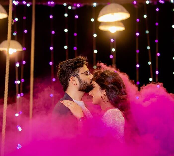 Couple sharing a romantic moment under fairy lights and colored smoke during a night Pre Wedding Shoot Timing in Jaipur.