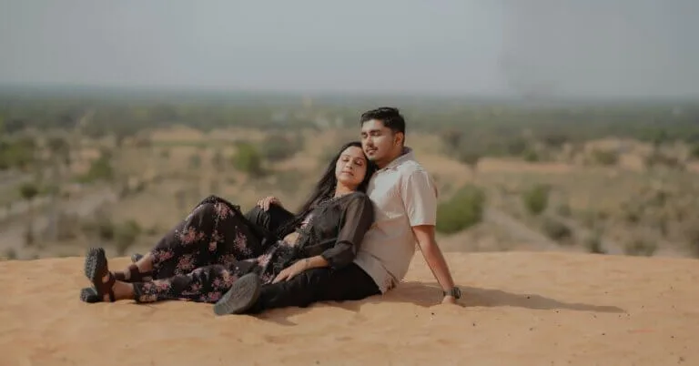 Couple posing for a romantic pre-wedding shoot near Jaipur with the woman wearing a flowing red gown against a soft sky background.