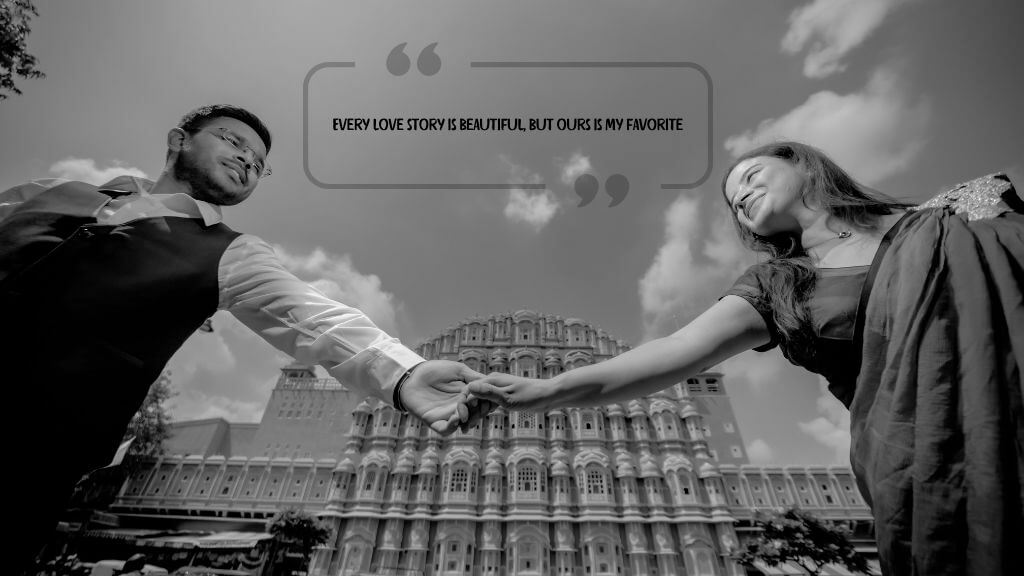 A couple holding hands and smiling in front of Hawa Mahal, Jaipur, with the romantic quote “Every love story is beautiful, but ours is my favorite” in a black and white wedding-themed photograph.

