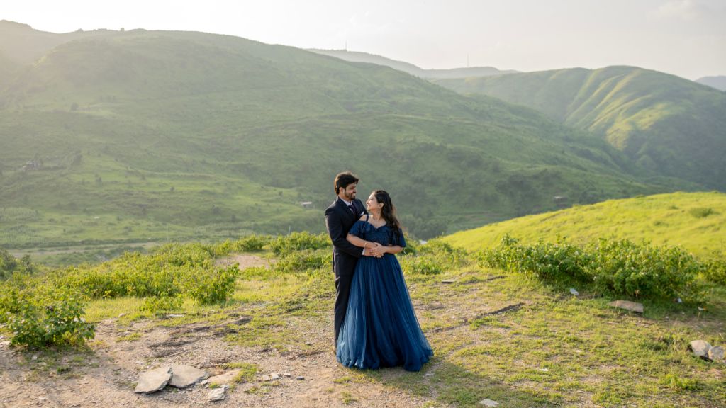 





























Couple embracing during a pre-wedding shoot in Udaipur with a stunning view of green hills and natural landscape
