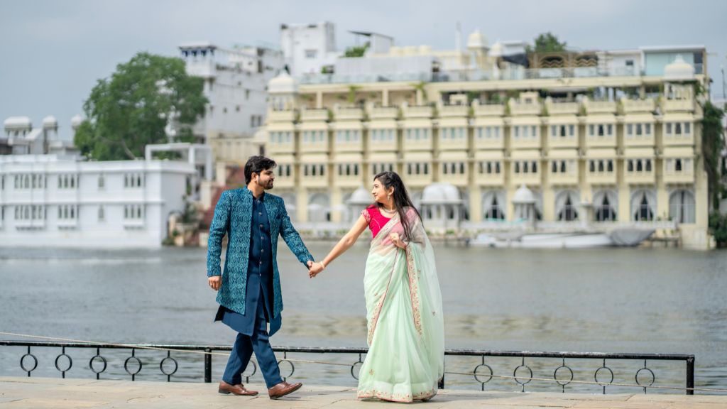 Couple walking hand in hand during a pre-wedding shoot in Udaipur with Lake Pichola and heritage palace backdrop