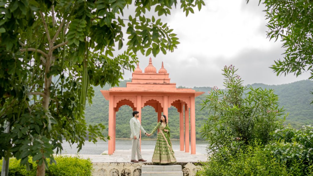 Couple posing during a pre-wedding shoot in Udaipur at a traditional pavilion surrounded by greenery and lake view