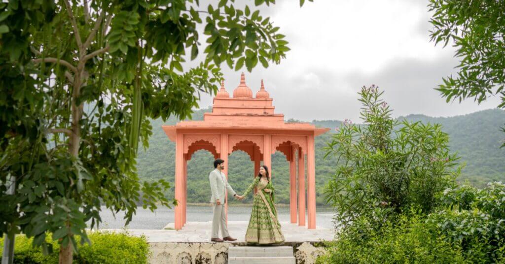 Couple holding hands during a pre-wedding shoot in Udaipur at a pavilion surrounded by greenery and lake views