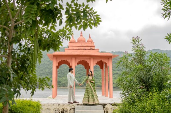 Couple holding hands during a pre-wedding shoot in Udaipur at a pavilion surrounded by greenery and lake views