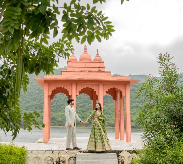 Couple holding hands during a pre-wedding shoot in Udaipur at a pavilion surrounded by greenery and lake views