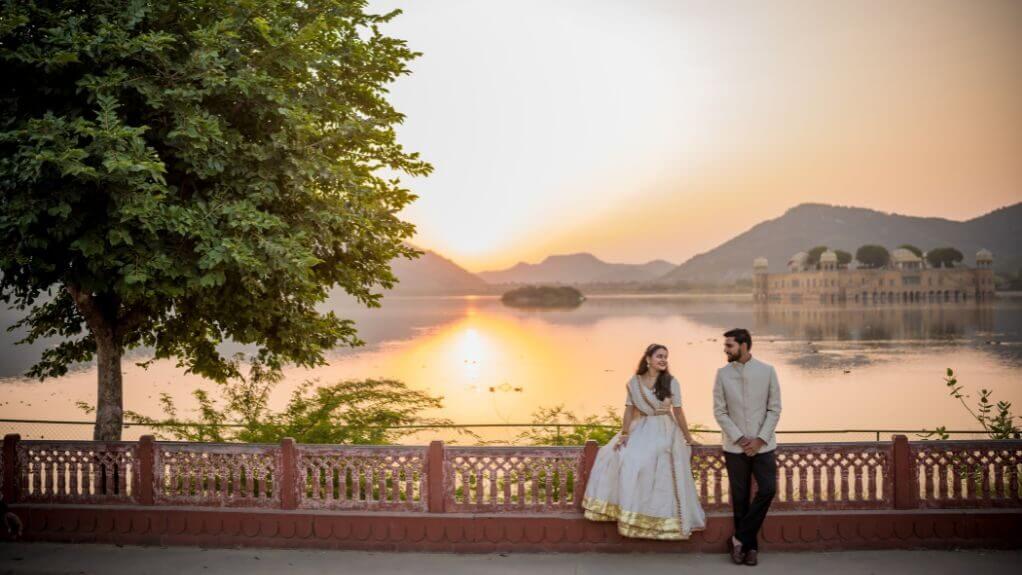 A romantic couple leaning on a railing with the Jal Mahal and Man Sagar Lake in the background during a sunrise Pre Wedding Shoot in Jaipur.