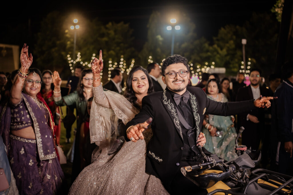 A joyful bride and groom making a grand nighttime entrance on a yellow ATV, surrounded by cheering guests and fairy lights, captured by Wedding Photographers in Jaipur.