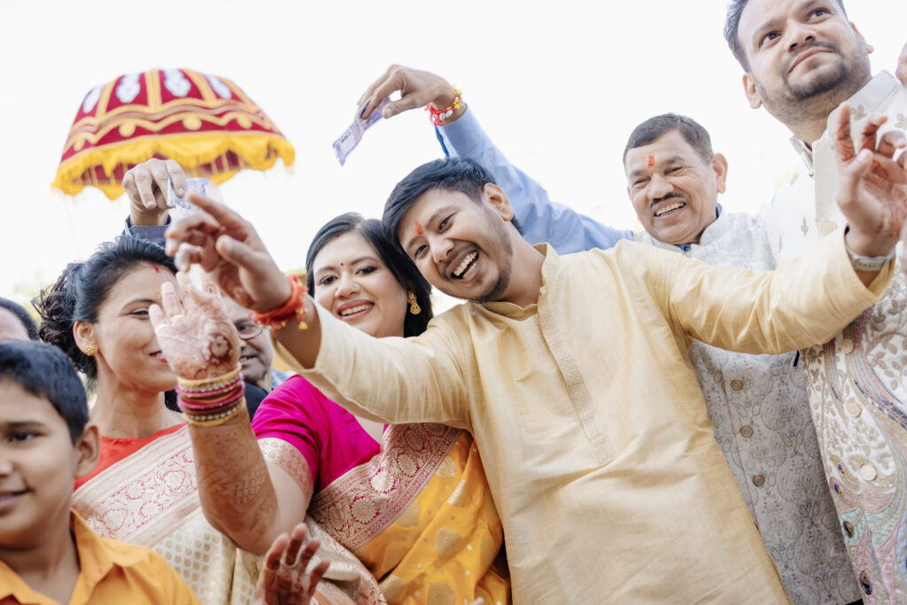 A candid shot of smiling family members tossing money and celebrating enthusiastically during a vibrant Indian wedding procession, captured by Wedding Photographers in Jaipur.