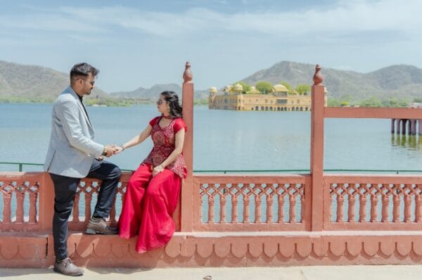 A couple standing together during their pre wedding photoshoot at Jal Mahal, Jaipur, with pigeons flying around them in a cinematic monochrome setting.
