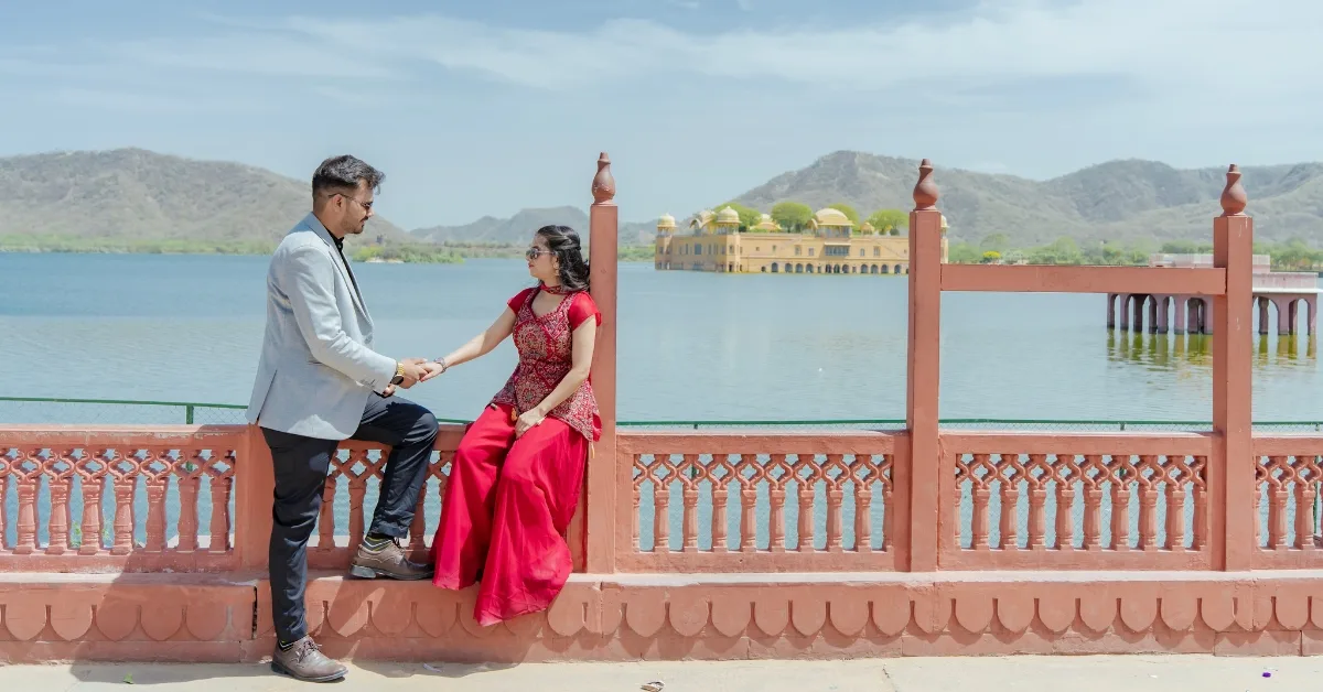 A couple standing together during their pre wedding photoshoot at Jal Mahal, Jaipur, with pigeons flying around them in a cinematic monochrome setting.